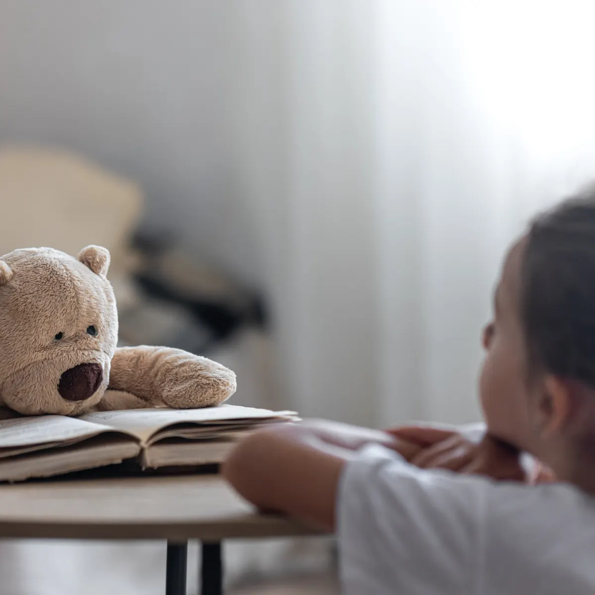 Niña leyendo con un peluche en una mesa